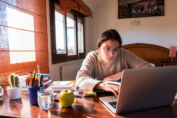 Young female student focused on her desk in the bedroom, studying at home with a laptop. Home concept.