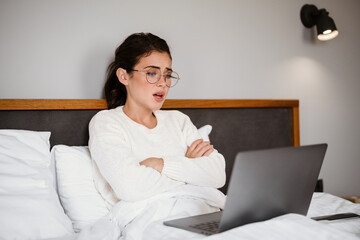 Unhappy brunette girl using laptop while sitting with arms crossed