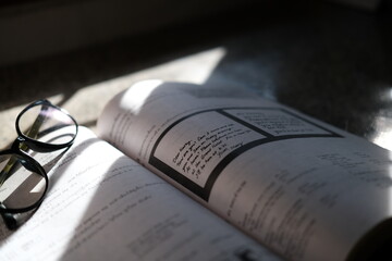 Books placed on the table with glasses and the light from the windows shines down, the books focus on the text