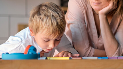 mom helping young son with laptop to do homework. Young woman teaching little boy to use the computer. baby sitter teaching little child girl use laptop application.