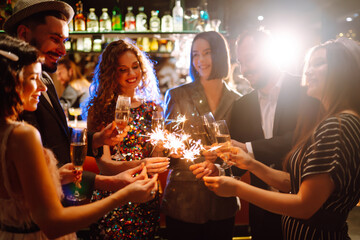 Group of happy people holding sparklers at the party. Young friends clinking glasses of champagne and enjoying new years eve with fireworks. Party, celebration, holidays concept.