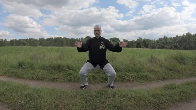 Man does exercises from Eastern martial practices. First, person slowly moves his hands, and then abruptly throws his hands in different directions