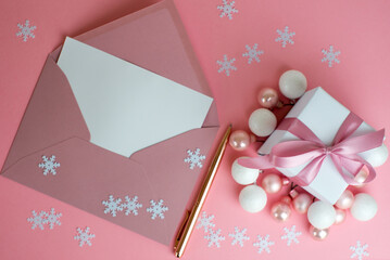 A pink gift, an empty envelope and a pen. Letter to St. Nicholas. Women's Christmas. Gift or present box with shiny balls, ribbons and snowflakes on pink background. Flat lay composition for christmas