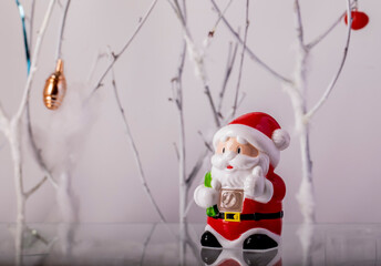 Toy Santa Claus with a bag of gifts on the background of a green Christmas tree and white trees.