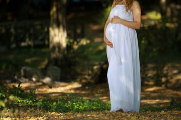Young pregnant female in a beautiful white dress doing a maternity photoshoot