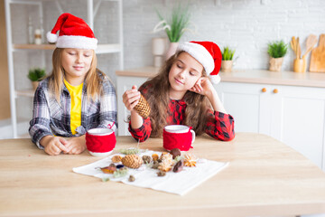 Merry Christmas and Happy Holidays! Cheerful cute kid girls having fun. Children in Santa hats have fun at breakfast in the morning. Loving family