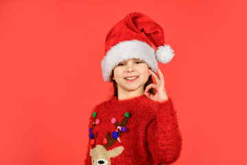 Can not hold back emotions. Counting days till christmas. Christmas party. Christmas holiday invitation. Adorable girl wear santa claus hat red background. Emotional face expression. Happy childhood