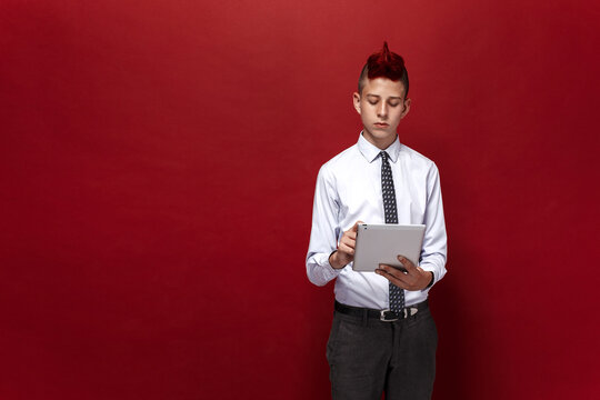 Portrait of red-haired teen punk with tablet against of red background. Isolated.