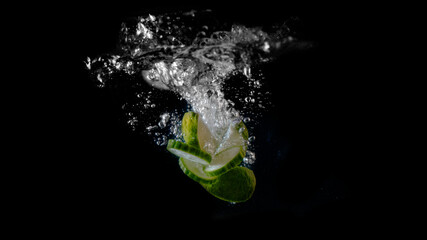 Fototapeta na wymiar Wedges of lime and slices of cucumber splash into a tank of water on a black background.