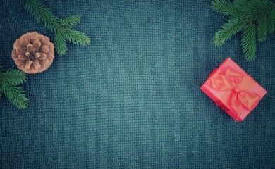Pine cone, red gift box and fir branch on green knitted sweater background. Christmas and new year composition with copy space