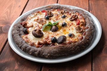 Pizza nera con impasto ai cereali e condita con mozzarella e funghi 