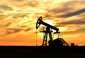 Crude oil pump jack at oilfield on atmospheric sunset backround. Fossil crude output and fuels oil production. Oil drill rig and drilling derrick. Global crude oil Prices, energy, petroleum demand