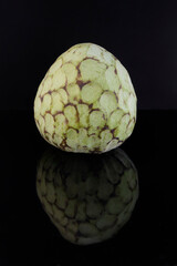 Obraz premium Custard apple reflected on a black glass table against black background