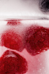 Vertical frame, frozen red raspberries and black currants inside ice