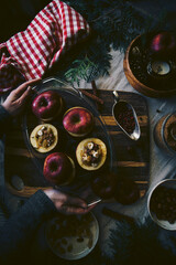 Process of making baked apples. Fresh red apples stuffed with hazelnuts, raisins, lingonberry and brown sugar on wooden board on Christmas table.