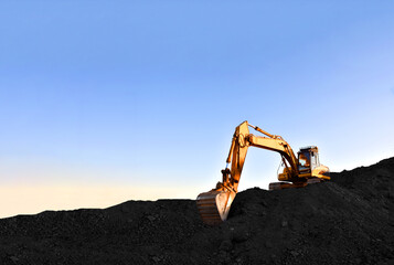Excavator during earthmoving at coal open pit on sunset background. Construction machinery and...
