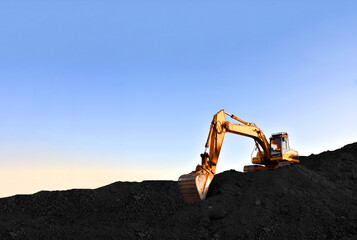 Excavator during earthmoving at coal open pit on sunset background. Construction machinery and earthworks heavy equipment for excavation at quarry. Recyclin and coal mining industry