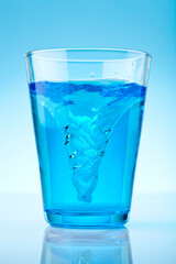 A blue glass with water swirling. Studio photo on blue background.