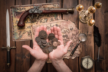 Pirate holding in hands an ancient treasure coins on a old treasure map on the table background.