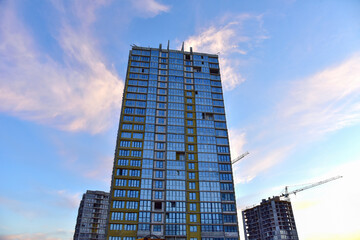 Mineral wool insulation of the facade building on construction site. Thermal protection of house. Installation double-glazed windows with frames. Tower cranes in action. Modern buildings background