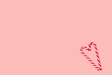 Christmas composition made of candy cane laid out in the shape of heart on a pink pastel background. Background made of food. Valentine's day and Christmas concept. Flat lay. Minimal composition