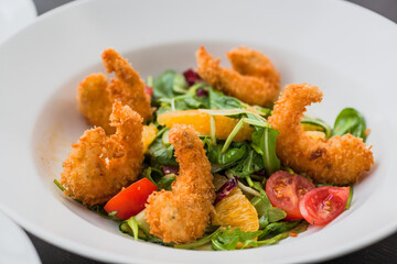 Salad with shrimp in crispy breadcrumbs, citrus mix, cherry tomatoes, fresh cucumber and orange-mustard sauce. Fresh food from restaurant menu