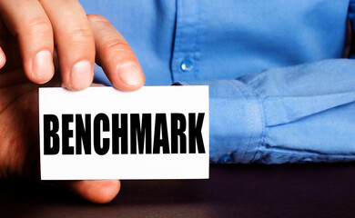 BENCHMARK is written on a white business card in a man's hand. Advertising concept