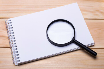 Blank notepad and magnifying glass on light wood background. Copy space