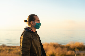 Man with hair bun and reusable face mask outdoors.