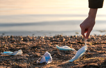 Man picking up used disposable medical face masks on the beach. The environmental problem after the coronavirus pandemic