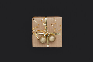 Christmas gift box or present decorated golden ribbon and two balls on black background.