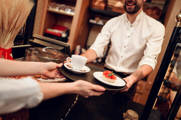Young Man Selling Cakes and Tea to Woman in Bakery