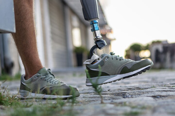 Low angle view at disabled young man with prosthetic leg walking along the street.