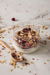 healthy and tasty granola with berries, fruits, nuts and yogurt in a glass dish with a wooden spoon on a light background