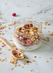 healthy and tasty granola with berries, fruits, nuts and yogurt in a glass dish with a wooden spoon on a light background