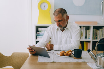 senior man using tablet computer while having breakfast at home