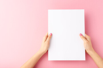 Woman’s hands holding empty white paper sheet on pink background. Close up