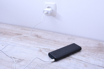 Black phone power bank plugged in the socket on the wall for charging on wooden background