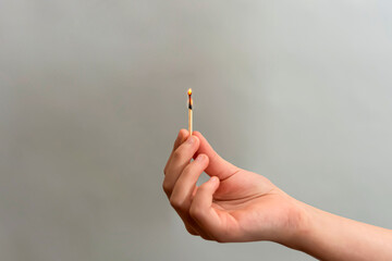 Girl holding a burning match with her hand on a gray background.