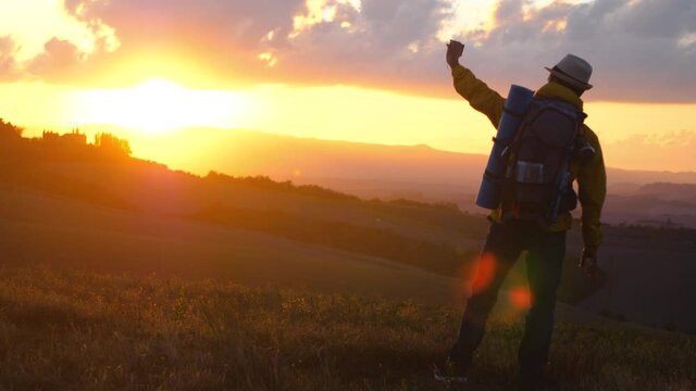 Man hiker with backpack taking pictures with smartphone in tuscany landscape at sunset. Hills in the countryside. Italy.