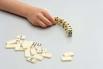 The girl is trying to neatly finish building a small wall with dominoes on a white table.
