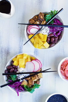 Vegan poke bowl with basmati rice, mango, fried tofu, purple cabbage, radishes, olives, pickled ginger and black sesame