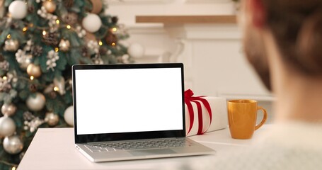 Over shoulder view of man speaking on video conference on laptop with Caucasian couple, Asian female and old Santa Claus man. Mixed-races friends and relatives speaking on holidays on multiple video