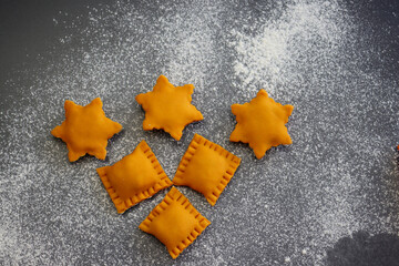 Raw Orange ravioli in the form of rectangles and stars on a background of scattered flour. Orange...