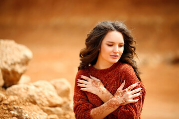 Henna Mehndi. Mehendi on hands. Outdoor portrait of attractive woman in sweater with curly hair.
