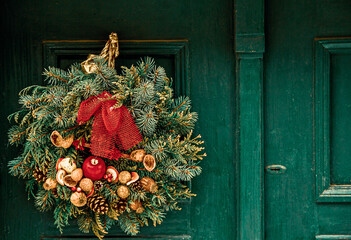 Christmas wreath with fir branches, cones, apples and nuts hangs on a green wooden door. Town house exterior, decorated for Christmas. © Yana