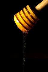Close-up of round wooden spoon with honey falling, illuminated, on black background, vertical