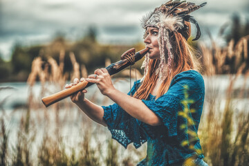 beautiful shamanic girl playing on shaman flute in the nature. - obrazy, fototapety, plakaty