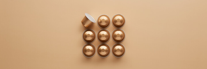 Caffeine, hot drinks and objects concept - close up of golden capsules or pods for coffee mashine on beige background. Top view with space for text. Flat lay..