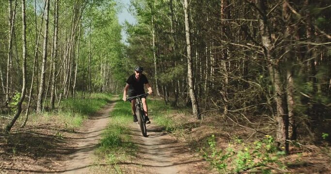Cyclist rides on a forest road. Man on a mountain bike rides in the forest. Adult man in a bicycle helmet rides on a mtb bicycle in the summer.